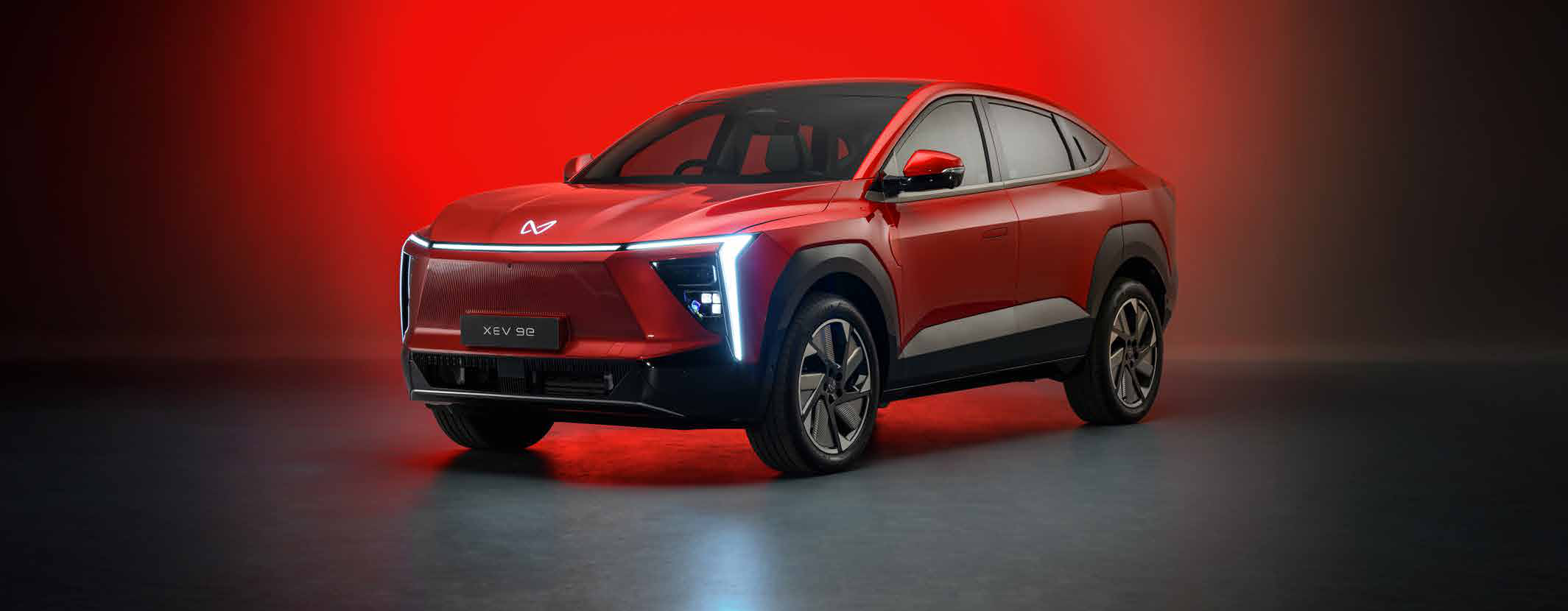 Mahindra XEV 9e — Suave SUV coupe design with a full-width LED light bar and illuminated logo
